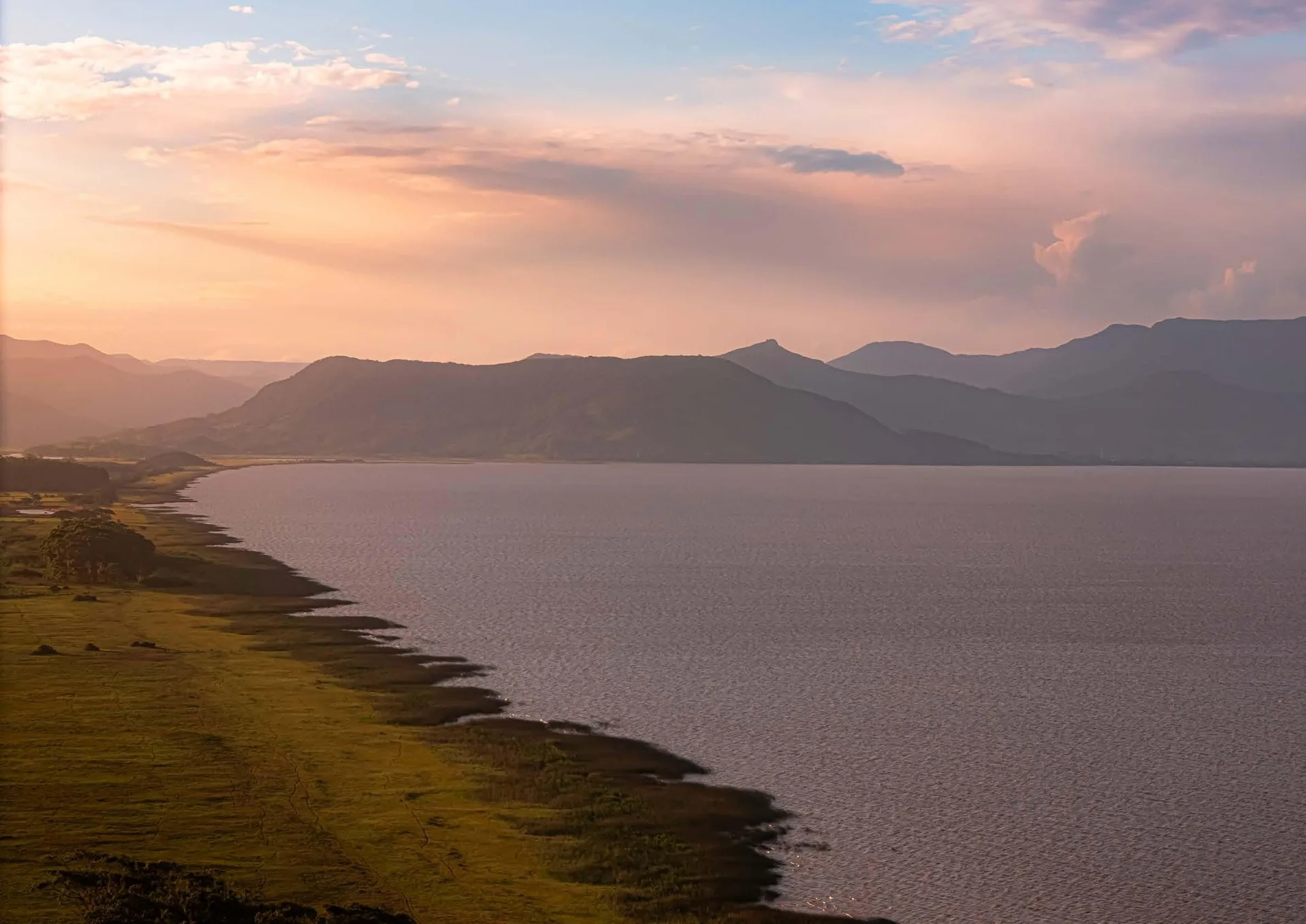 Foto aérea da lagoa ao pôr do sol, com a serra ao fundo, na região do AVA Residences em Maquiné