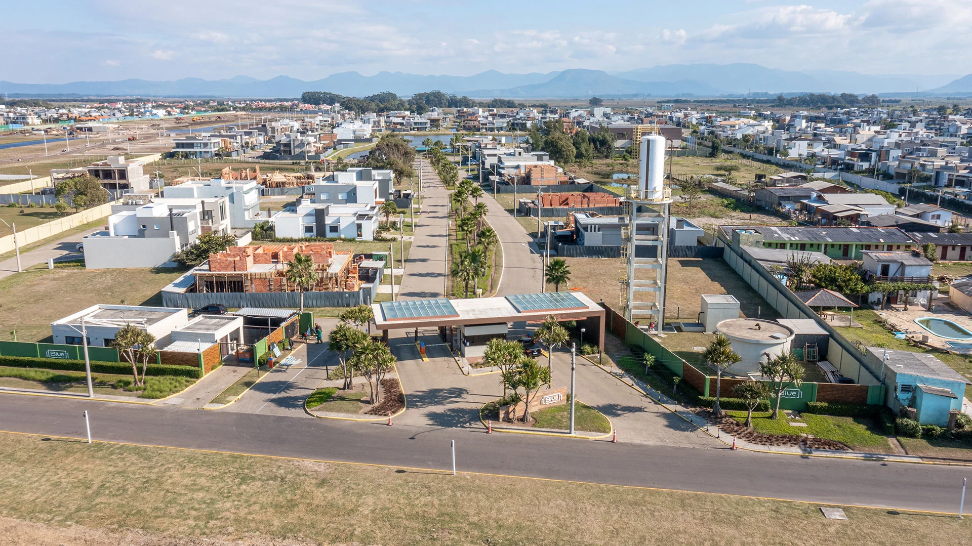 Foto aérea do pórtico de acesso do Blue Xangri-lá com a guarita e a avenida arborizada de entrada