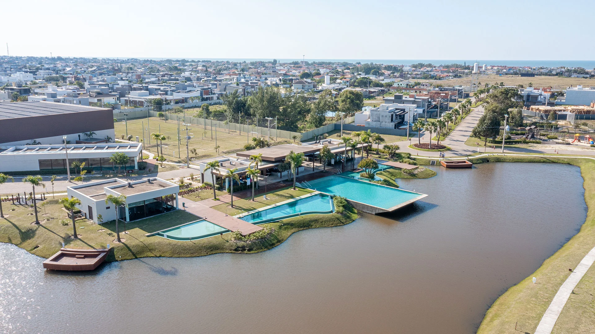 Foto aérea da quadra gramada do Blue Xangri-lá com o clube e o mar ao fundo