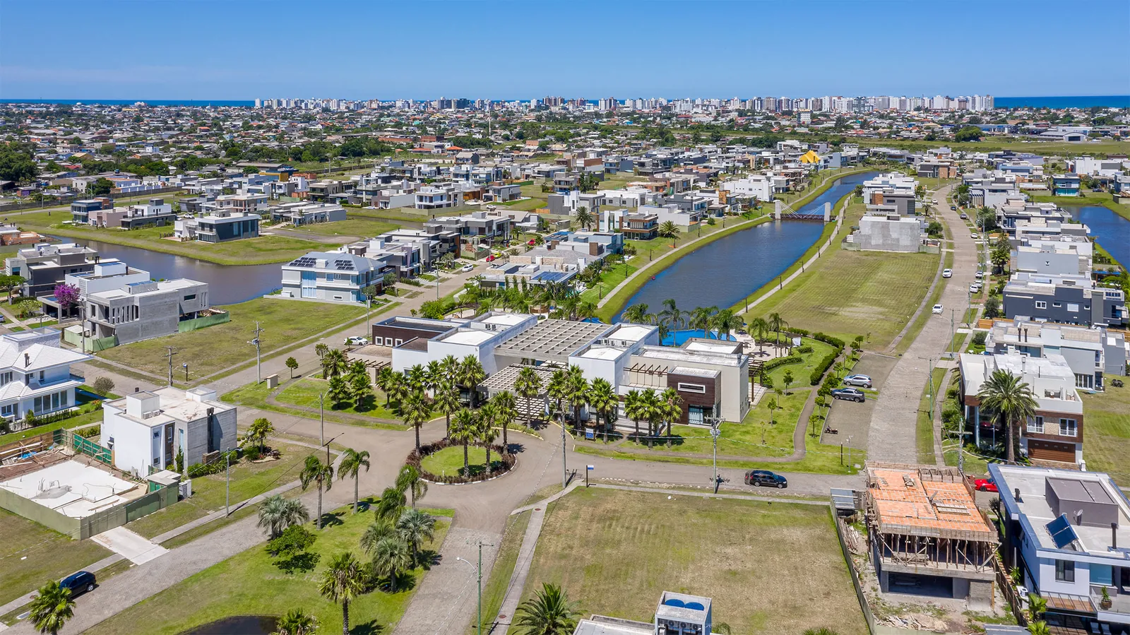 Foto aérea dos canais internos do Capão Ilhas Resort cortando o bairro residencial, com casas nas duas margens, um dos clubes ao fundo e o mar no horizonte