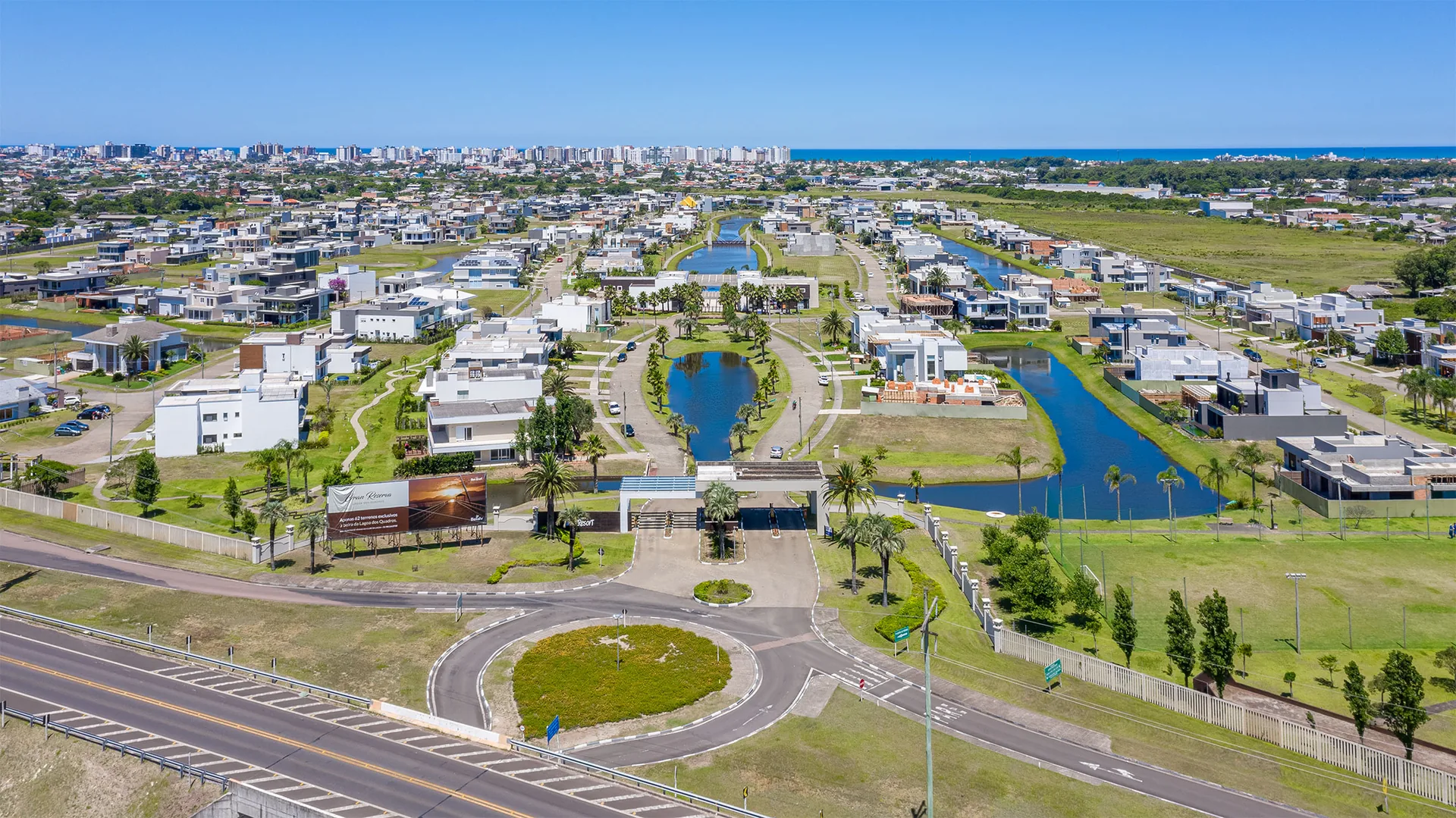 Foto aérea do Capão Ilhas Resort com o pórtico de entrada, os canais internos e o skyline de Capão da Canoa ao fundo
