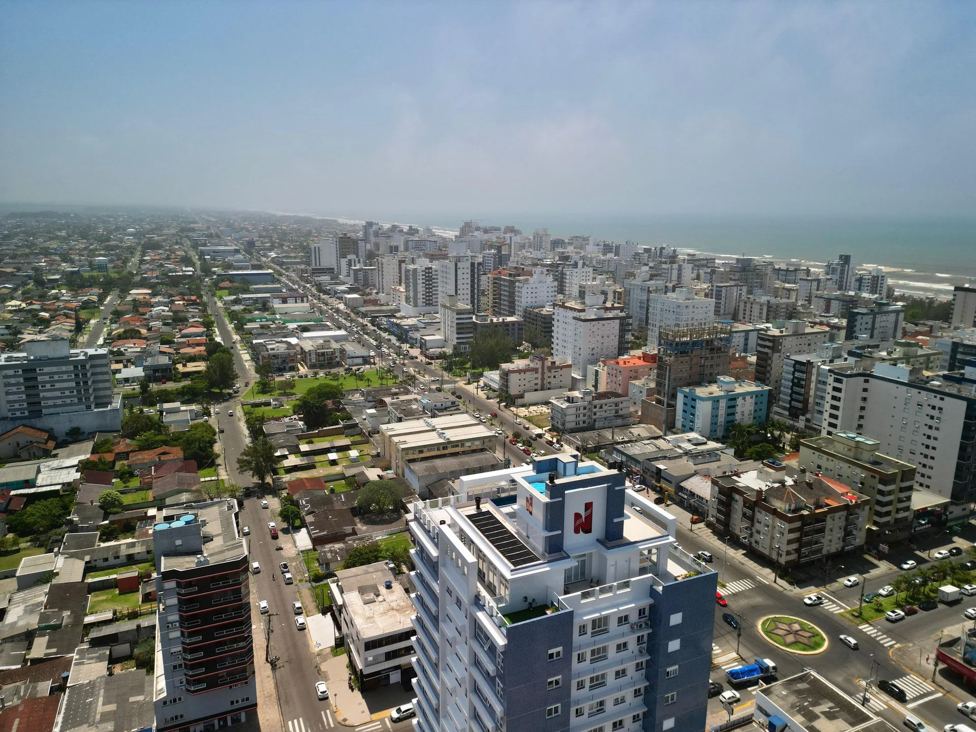 Vista aérea real da torre azul-marinho e branca do Domênico Home & Club, inserida no tecido urbano de Capão da Canoa
