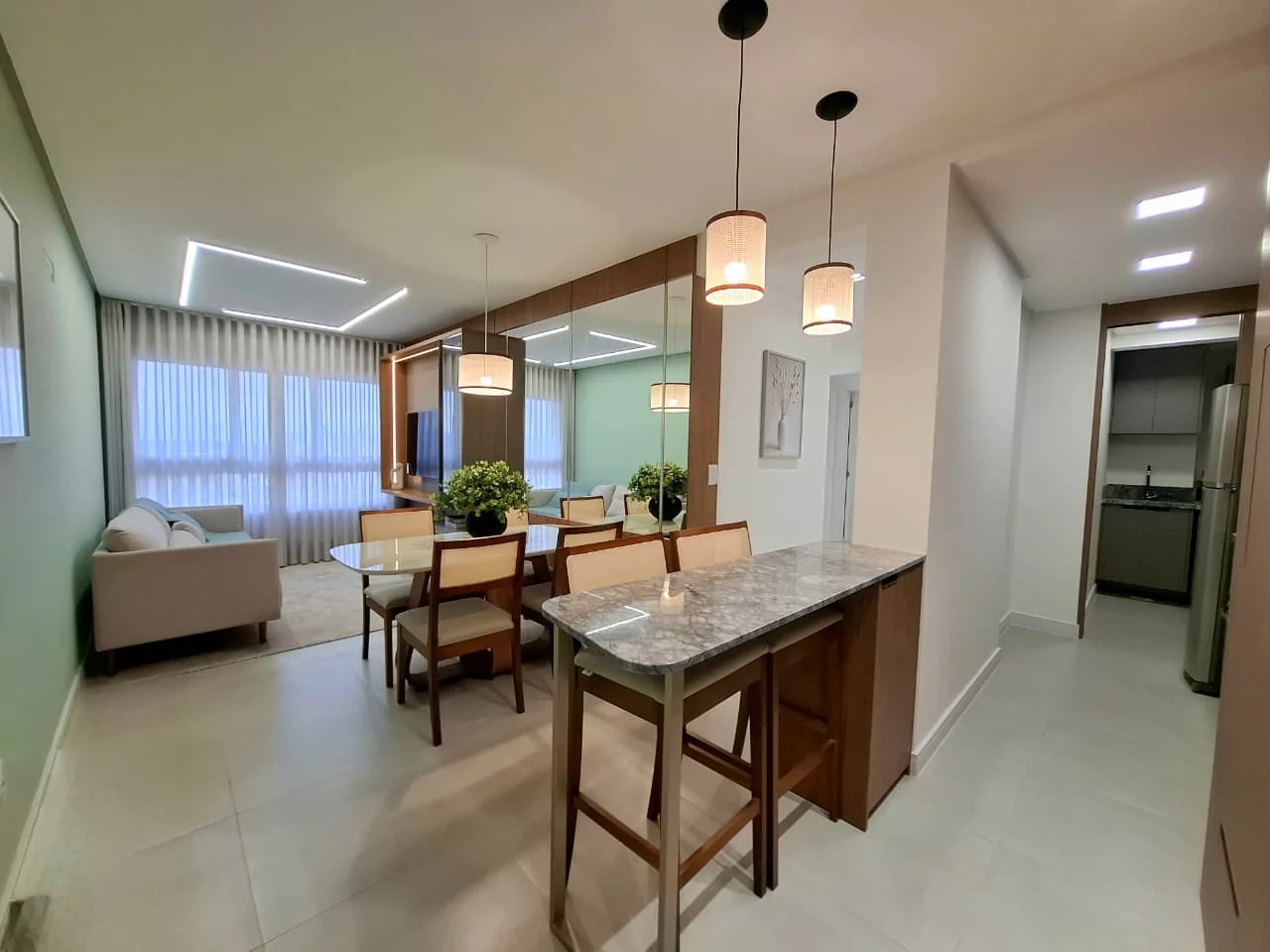 Living do apartamento decorado do Domênico Home & Club, com sofá, mesa de jantar para quatro lugares e ilha com banquetas diante da cozinha americana