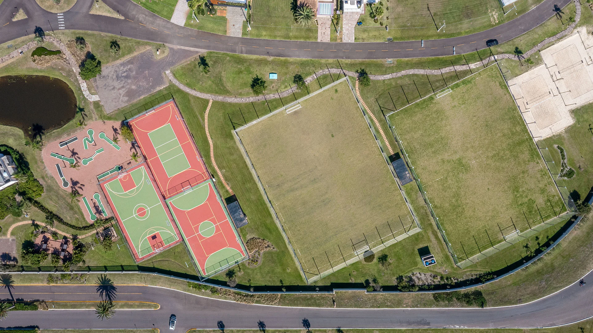 Foto aérea vertical do complexo esportivo do Enseada Lagos, com campos de futebol society, quadras poliesportivas, quadras de areia e minigolfe