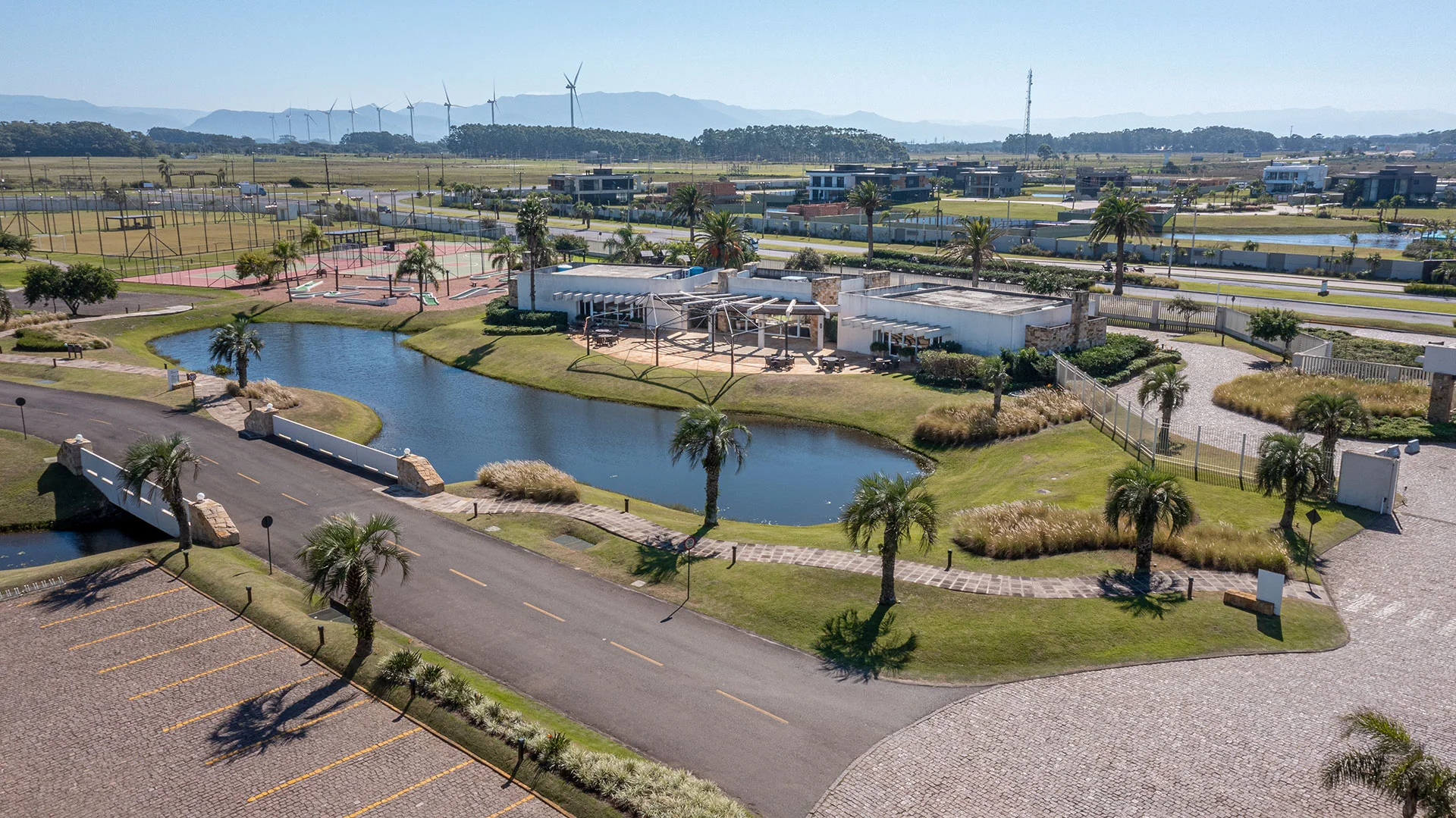 Foto do paisagismo interno do Enseada Lagos, com ponte, palmeiras adultas e calçamento de pedra