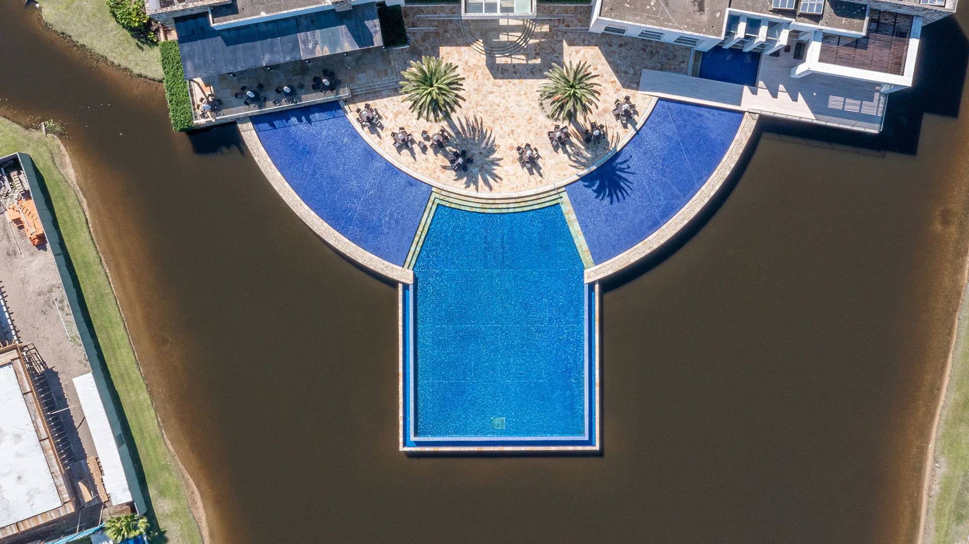 Foto aérea vertical da piscina do club house do Enseada Lagos projetada sobre o lago