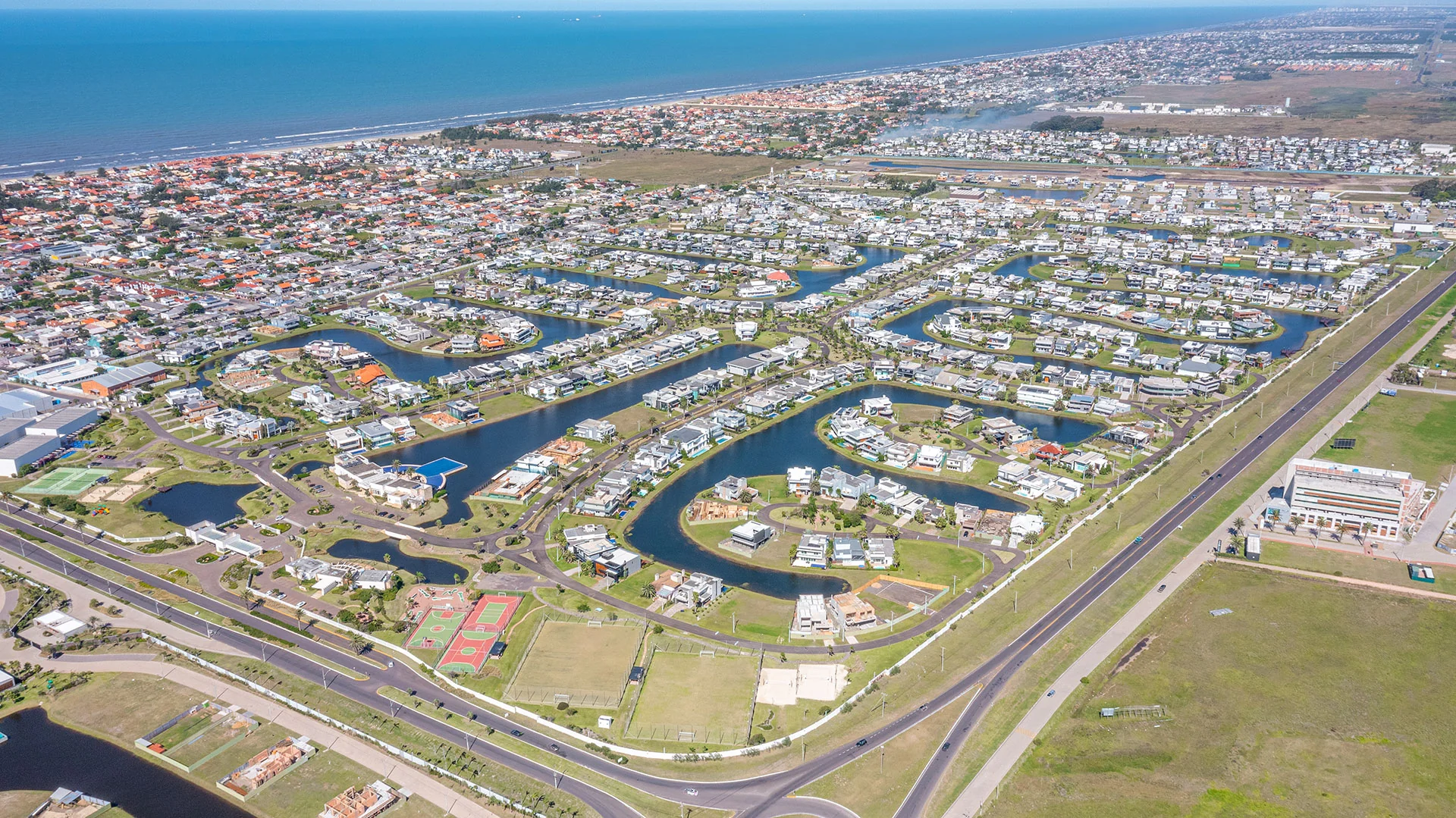 Foto aérea do Enseada Lagos de Xangri-Lá e do entorno urbano, com o mar de Xangri-Lá ao fundo