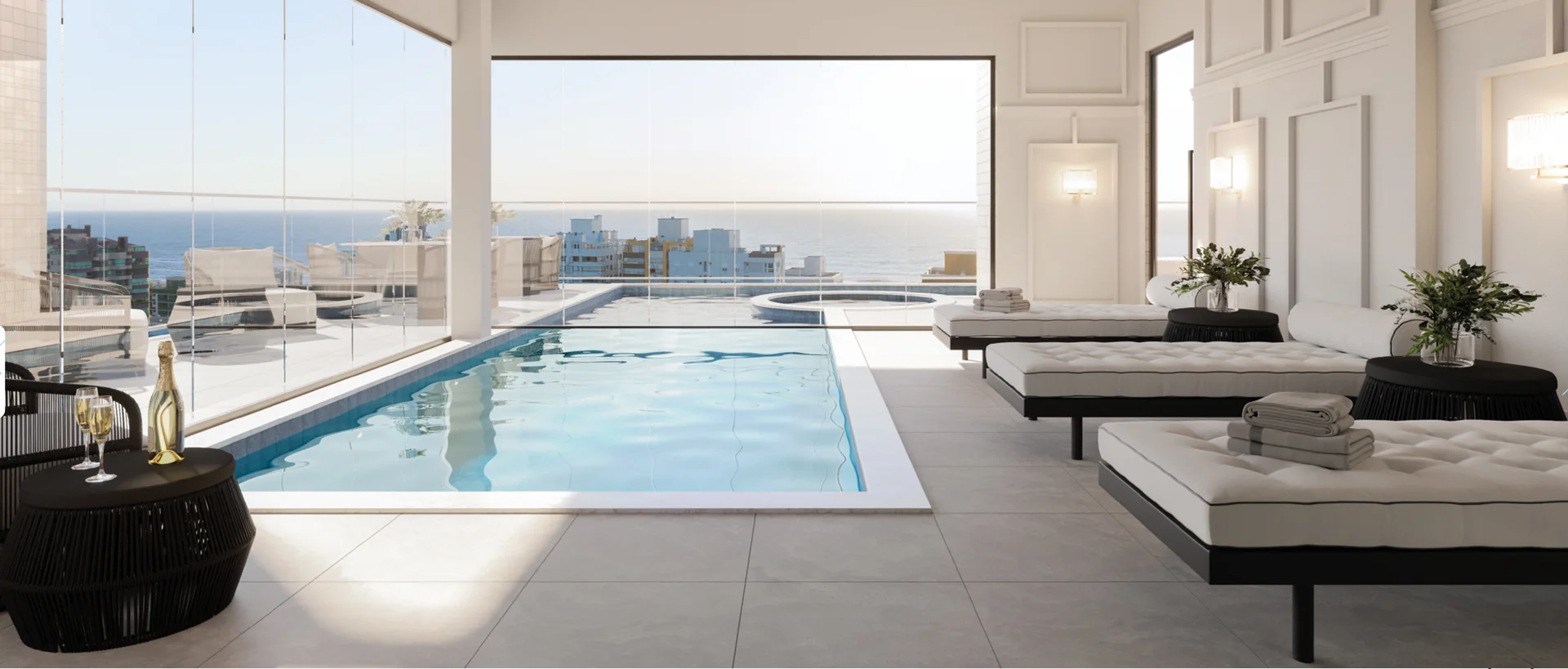 Piscina interna aquecida do Four Seasons Residence, com espreguiçadeiras e o mar visto pelo fechamento em vidro