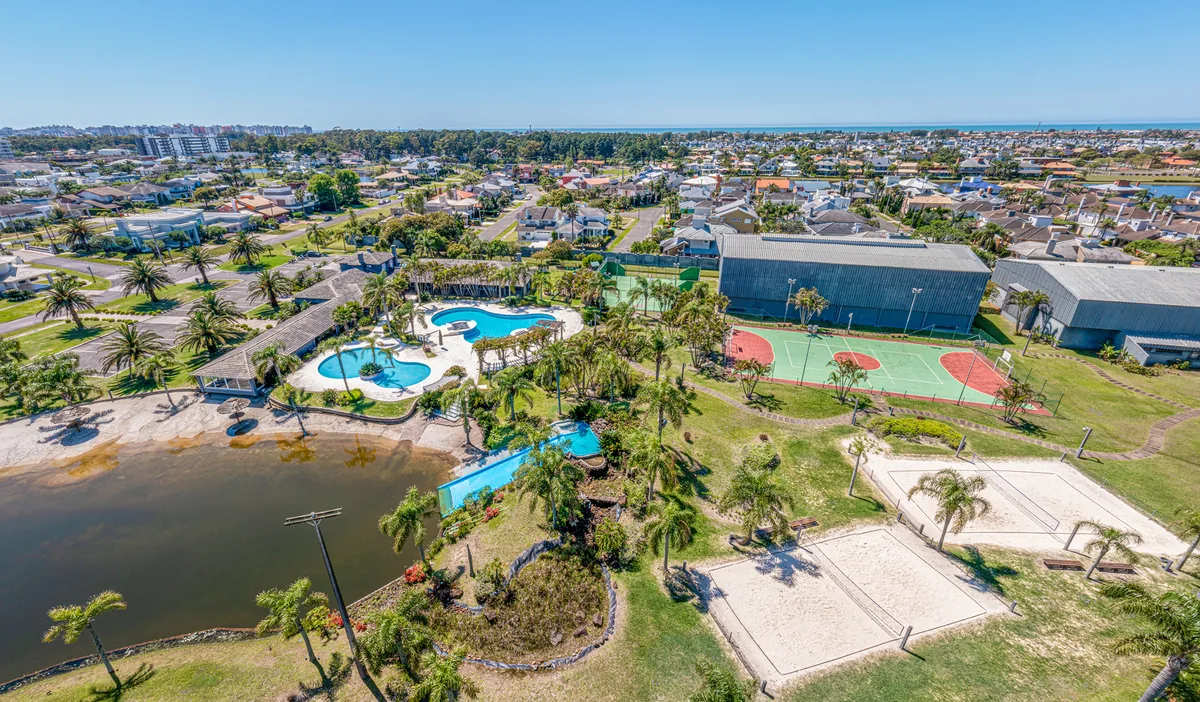 Vista aérea do clube central do Atlântida Ilhas Park, com piscinas em formato orgânico, praia artificial de areia, toboágua e quadras esportivas junto ao lago