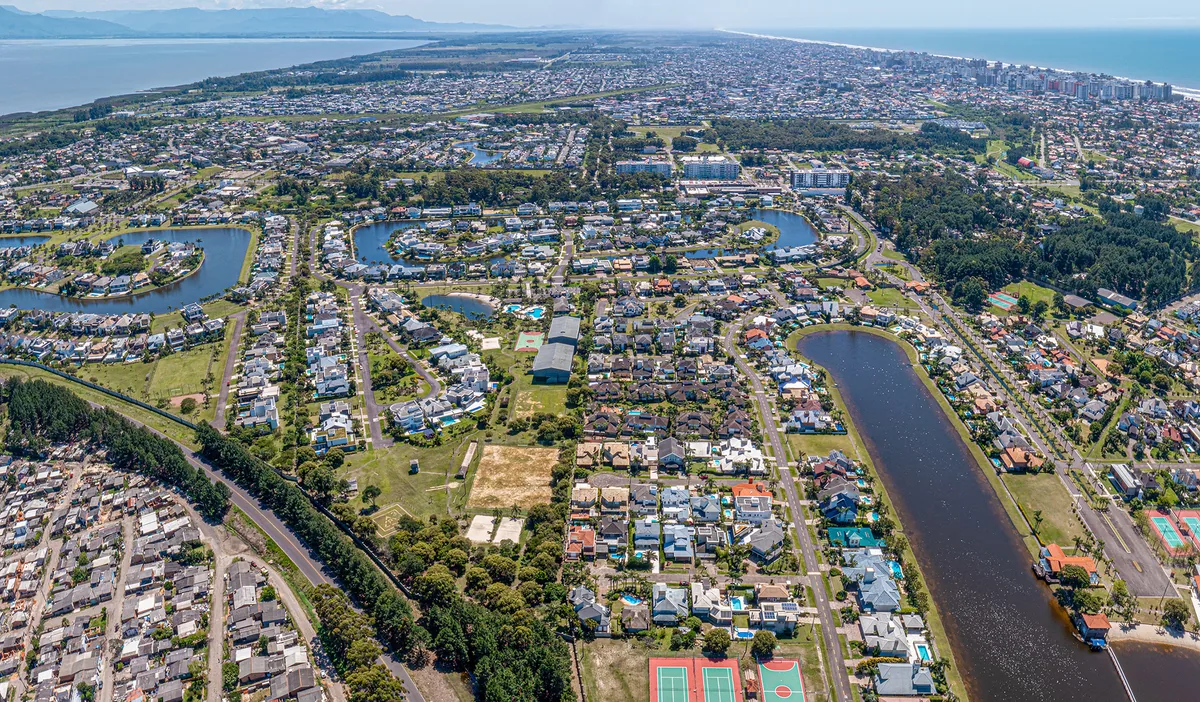 Vista aérea ampla do balneário de Atlântida, em Xangri-Lá, com o sistema de lagos e canais internos do Atlântida Ilhas Park, o mar, a lagoa e a serra ao fundo