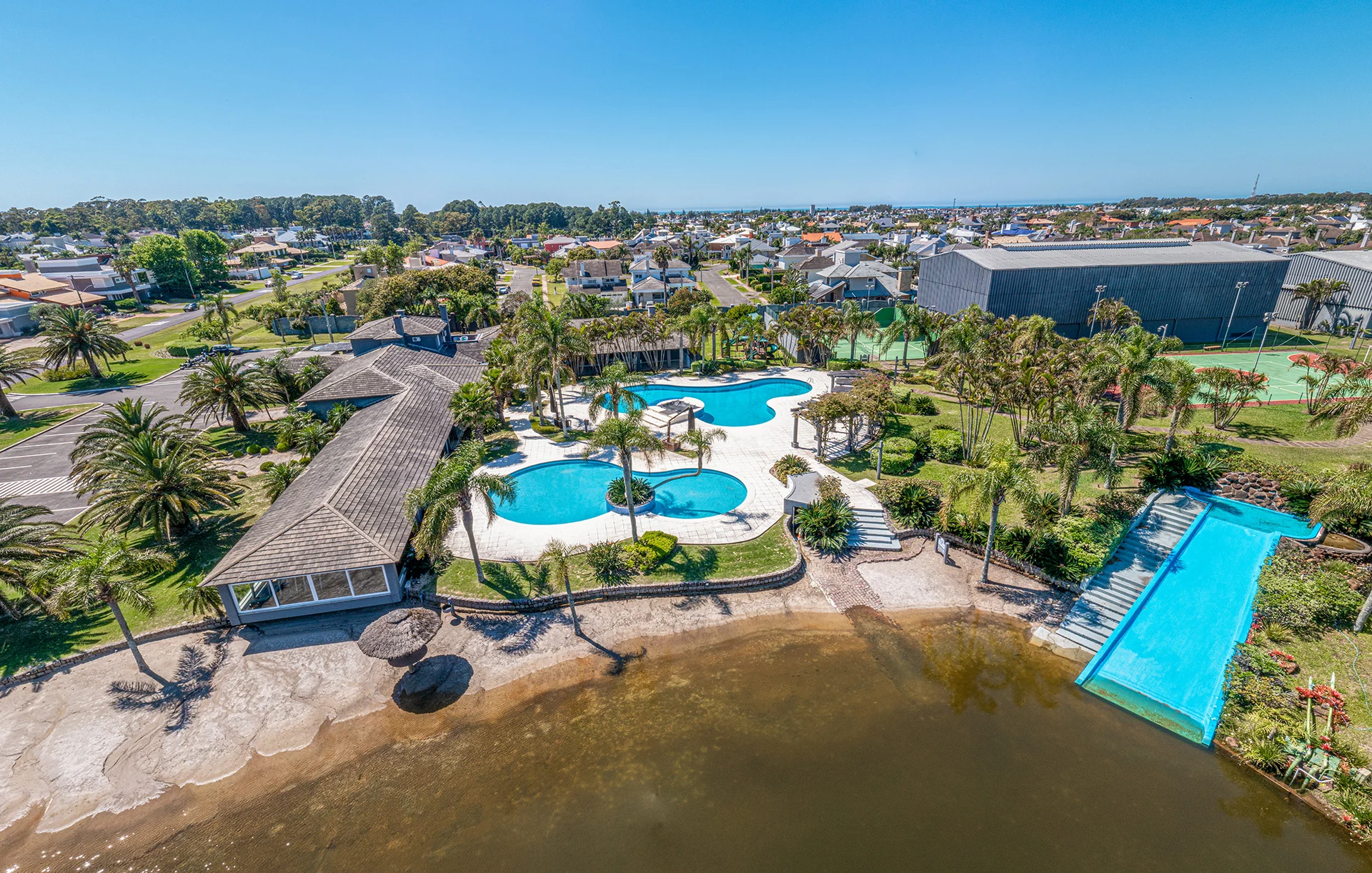 Foto aérea do clube central do Atlântida Ilhas Park com piscinas, praia artificial, toboágua e quadras esportivas, cercado pelos canais internos