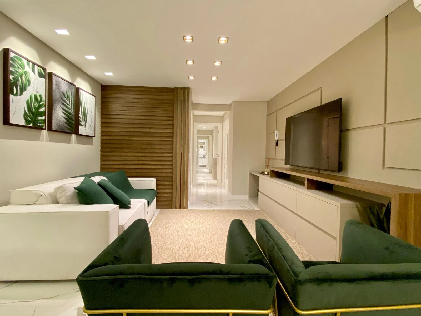 Sala de estar decorada do apartamento 401 do Edifício João Alves Diniz, com sofá branco, poltronas verdes e painel ripado de madeira
