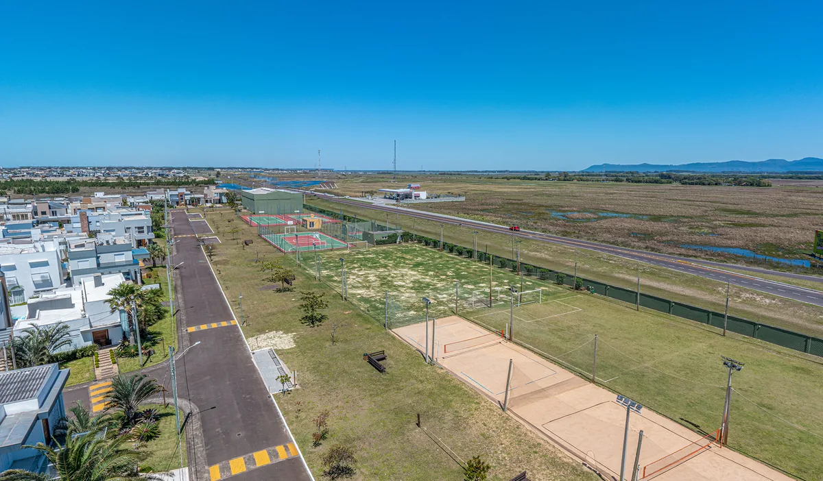 Quadra de vôlei de areia do Las Palmas, também usada para beach tennis, com rede montada e campo de futebol ao lado