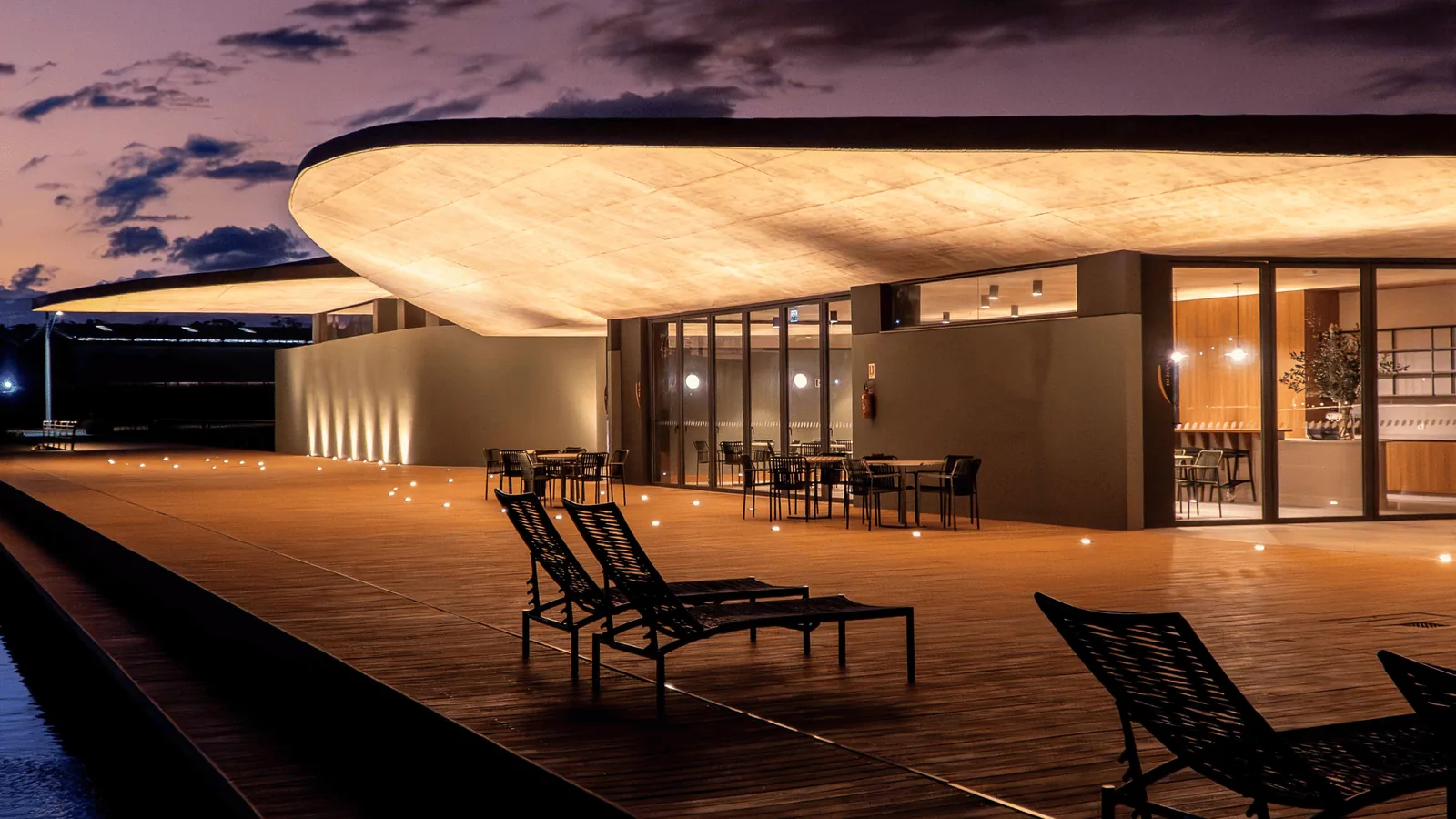 Deck e estar externo do clube do Lótus Atlântida voltado ao espelho d'água