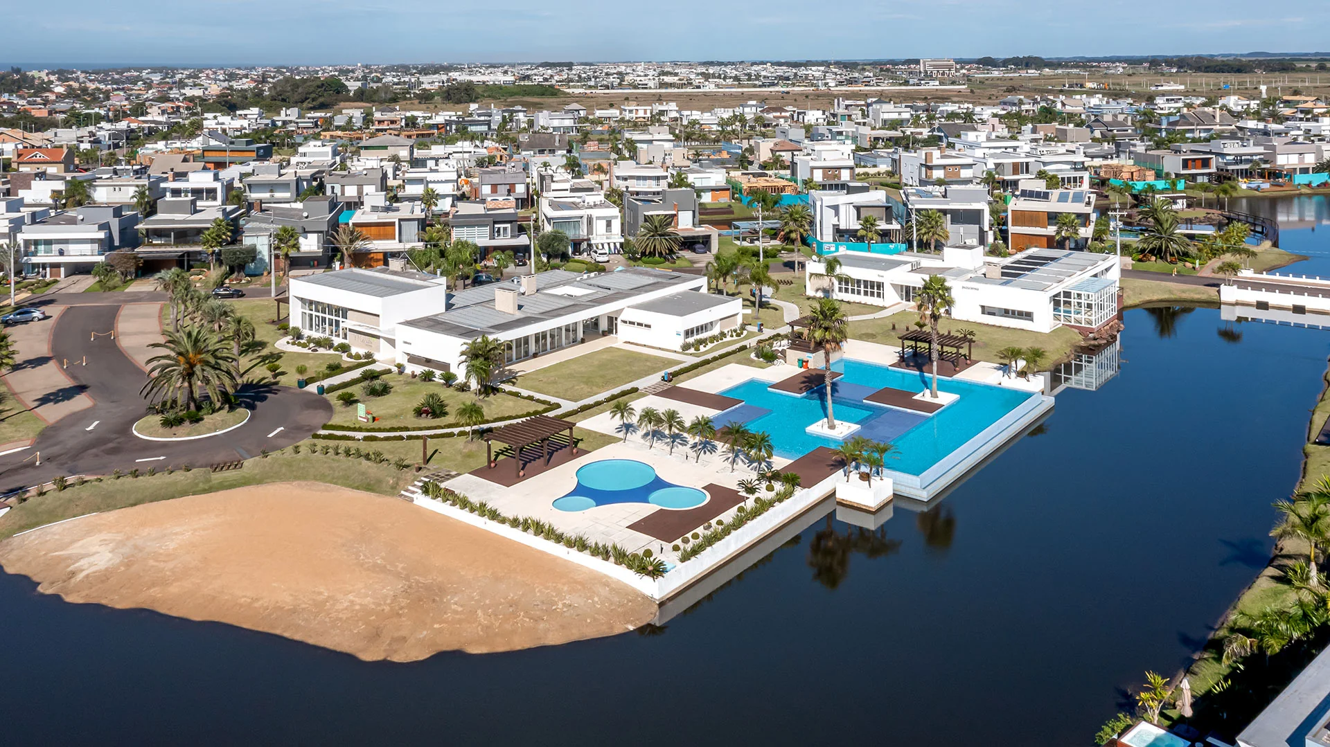 Foto aérea do clube do Malibu Beach Residence com piscinas, salão e lago ao redor