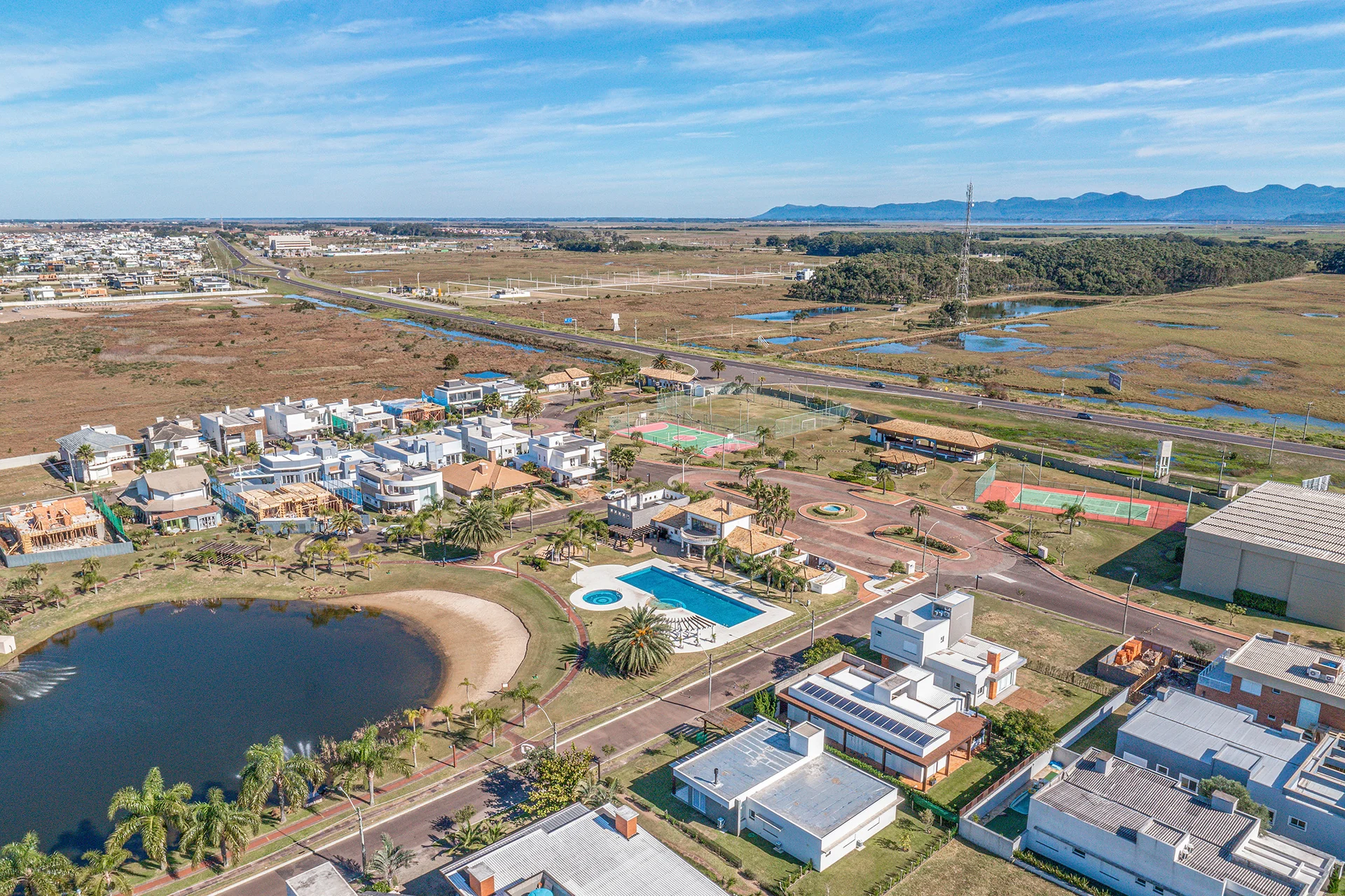Foto aérea da piscina do clube do Quintas do Lago, com playground, pergolado de madeira e o clubhouse ao fundo