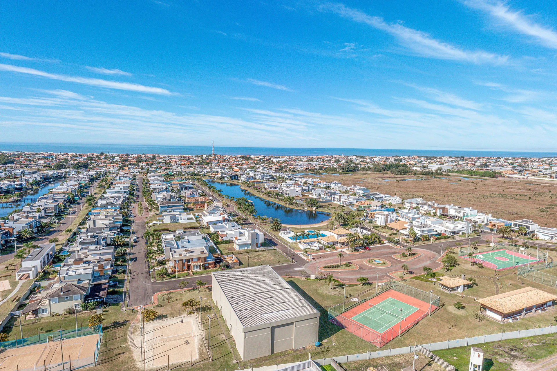 Foto aérea das quadras de tênis, quadra poliesportiva e ginásio de apoio do Quintas do Lago, com o mar ao fundo