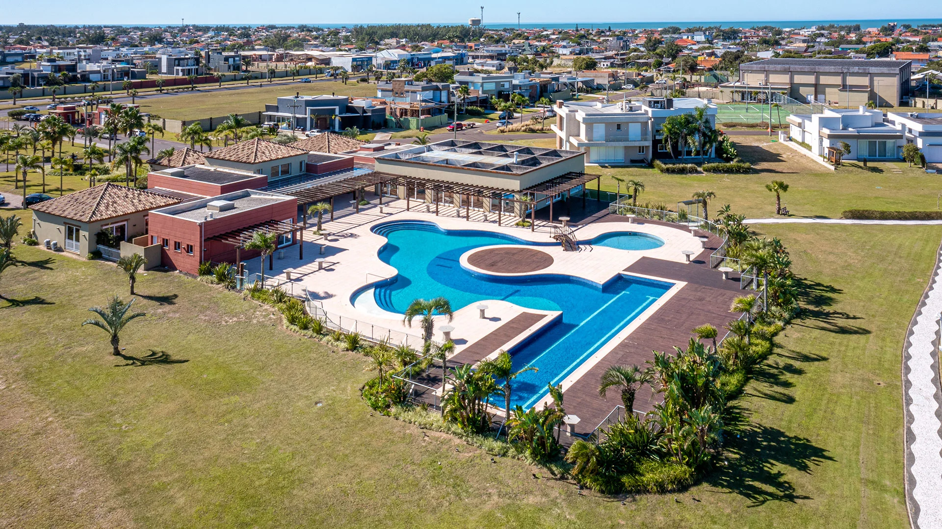 Foto aérea do prédio do clube do Riviera em estilo mediterrâneo, telhado colonial, com palmeiras e o mar ao fundo