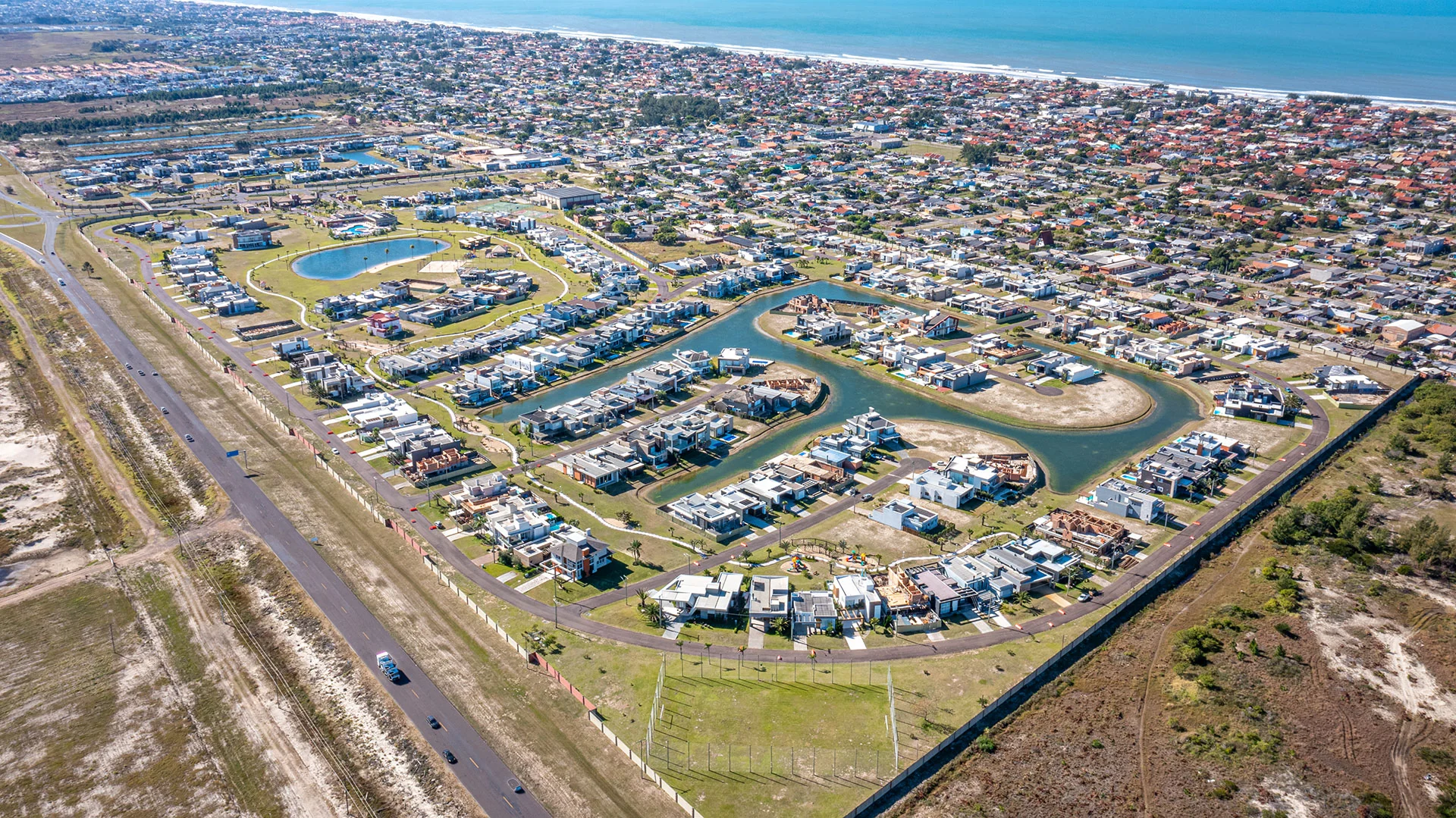Foto aérea do Riviera com o mar ao fundo, os lagos internos, o clube e a passarela que liga as duas fases, no bairro Rainha do Mar de Xangri-Lá