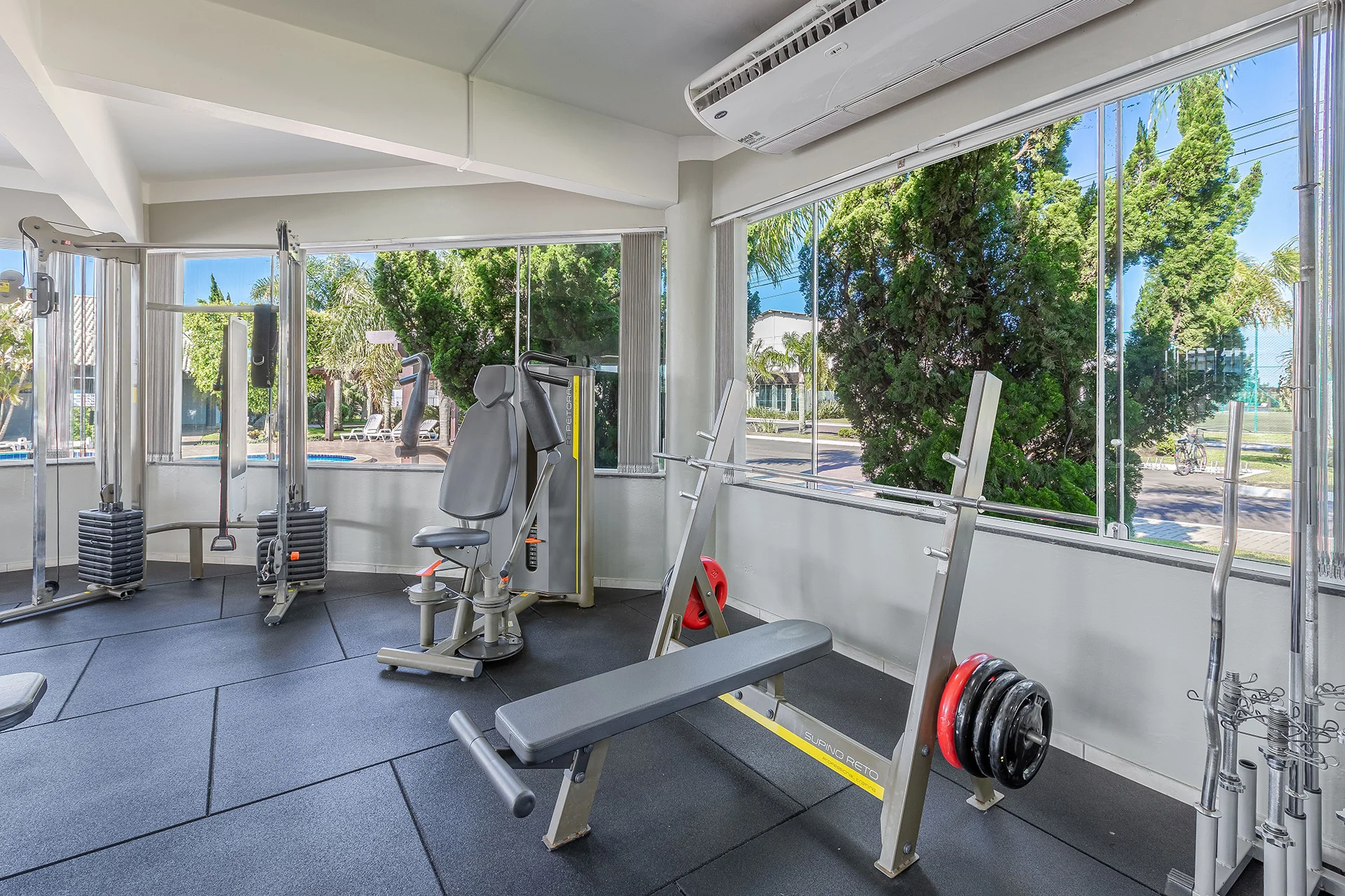 Foto da academia do Velas da Marina com equipamentos e vista para as piscinas e o canal